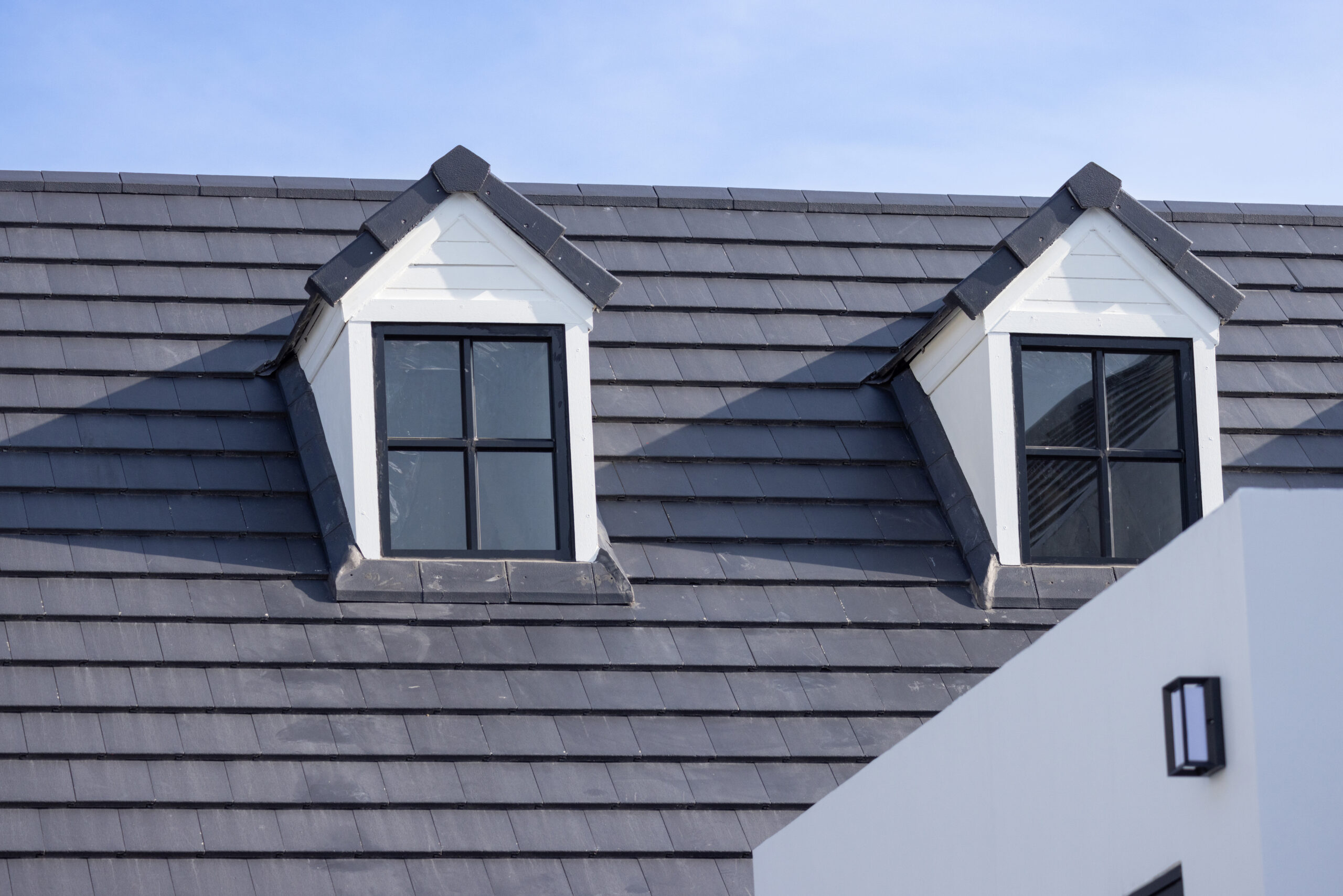 View of top of dark gray residential roof with two small windows with eaves