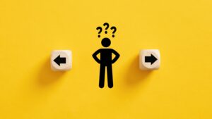 Graphic of a black stick figure with three question marks above his head on a yellow background; there’s a small wooden cube with an arrow facing outward on either side of him