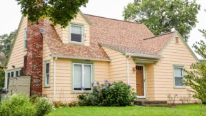Beautiful home exterior with yellow siding and brown asphalt shingle roof with brick chimney and well-kept front yard