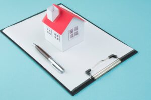 A miniature house sits on clipboard, symbolizing the need for a roof warranty.