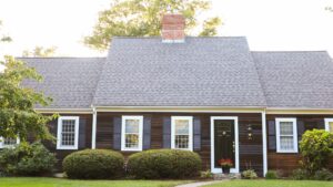Beautiful home with large, steep-sloped asphalt shingle roof, dark black siding, and windows with white frames and dark shutters